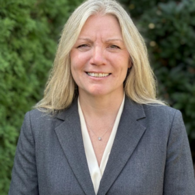 Woman with long blond hair, smiling in a in a grey suit